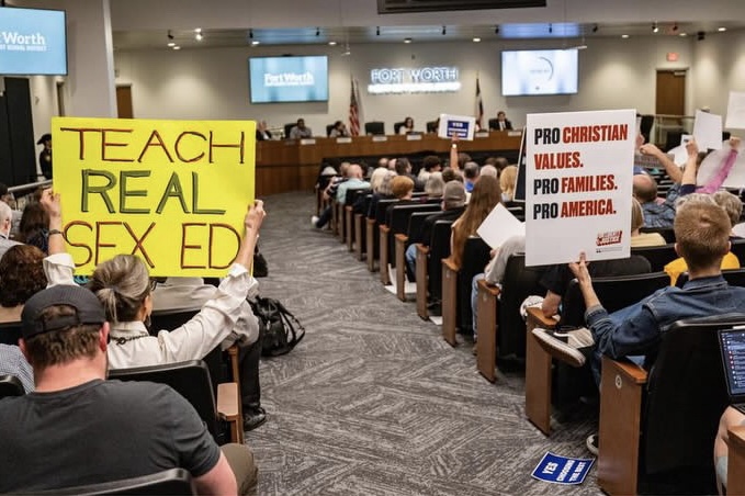 Two attendees of the February 27th FWISD school board meeting hold up opposing signs. 